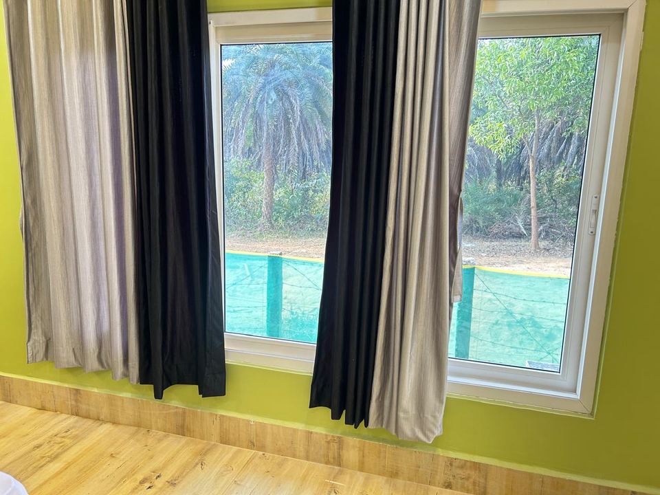 Cottage window with curtains open to trees beyond at Chamtaburu Eco Village, Ajodhya Hills